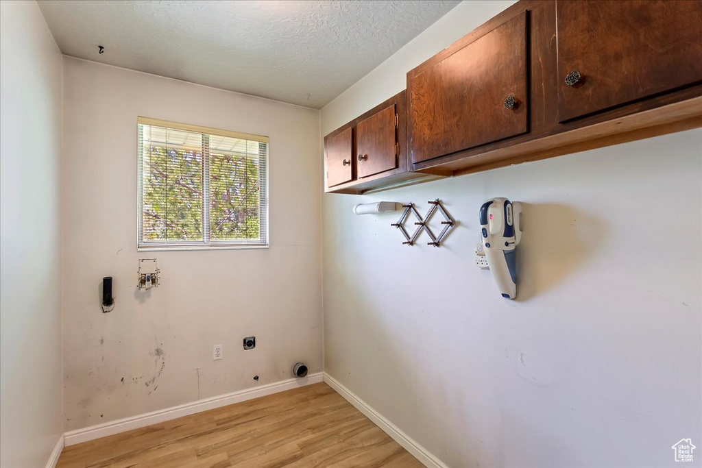 Laundry area featuring cabinet space, electric dryer hookup, light wood-style floors, hookup for a washing machine, and baseboards