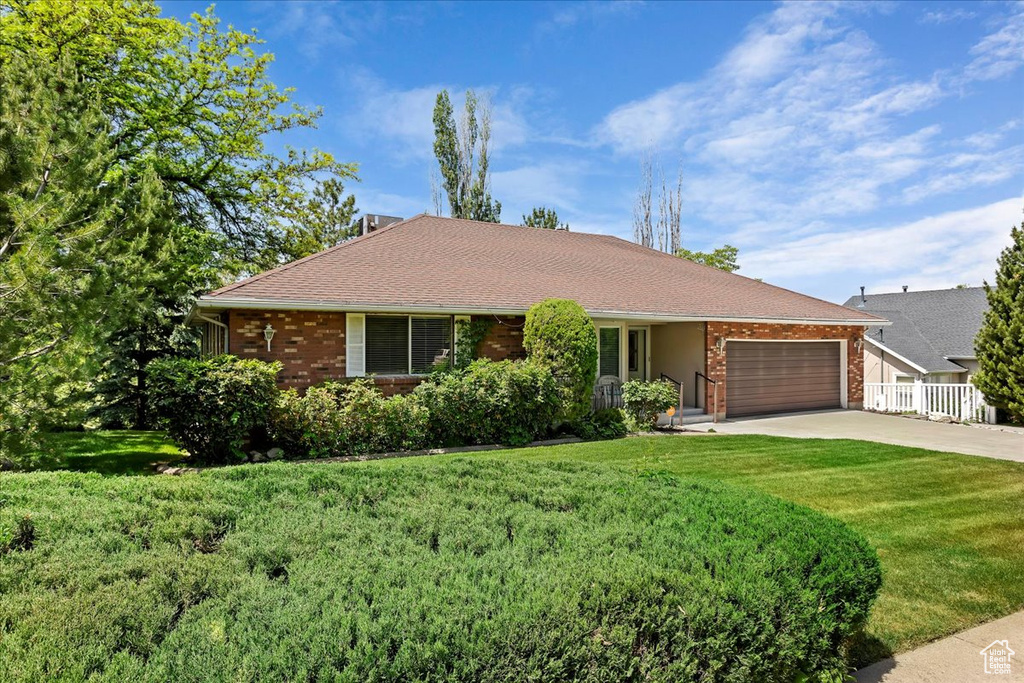 Ranch-style home featuring brick siding, a garage, a front yard, and driveway