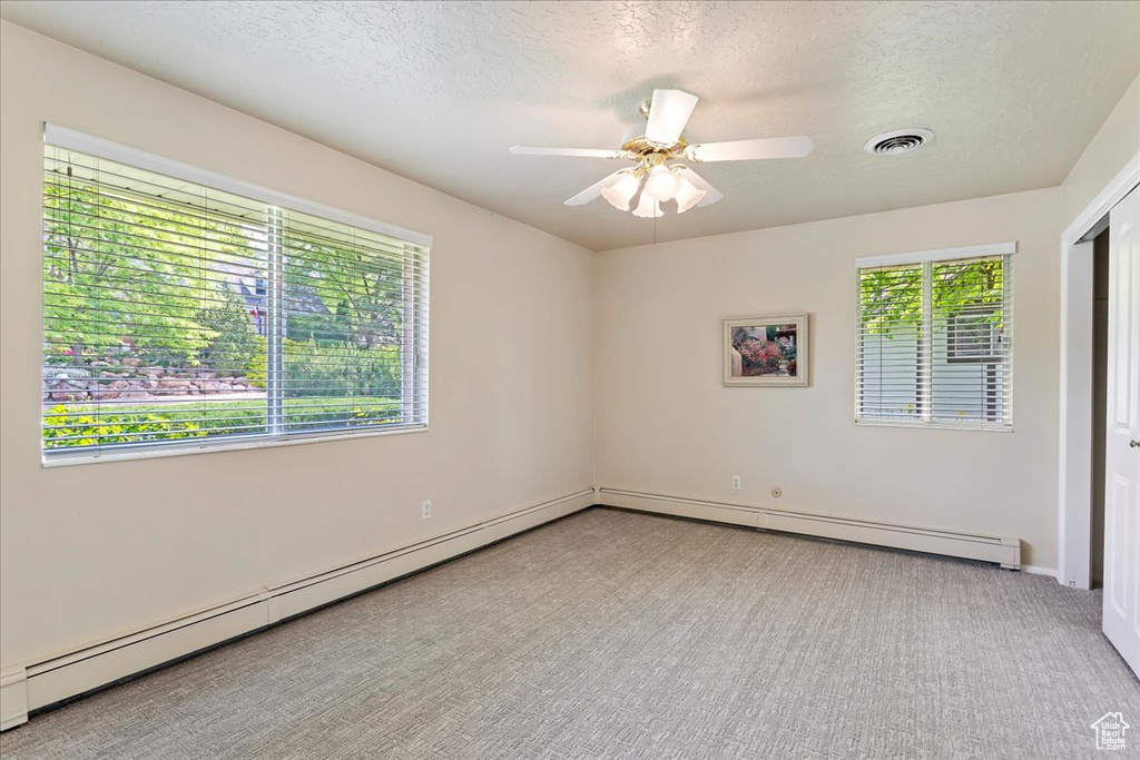 Carpeted empty room with a textured ceiling, a baseboard radiator, a ceiling fan, and baseboards