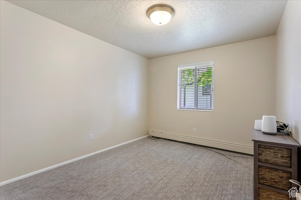Carpeted empty room with a baseboard radiator, a textured ceiling, and baseboards
