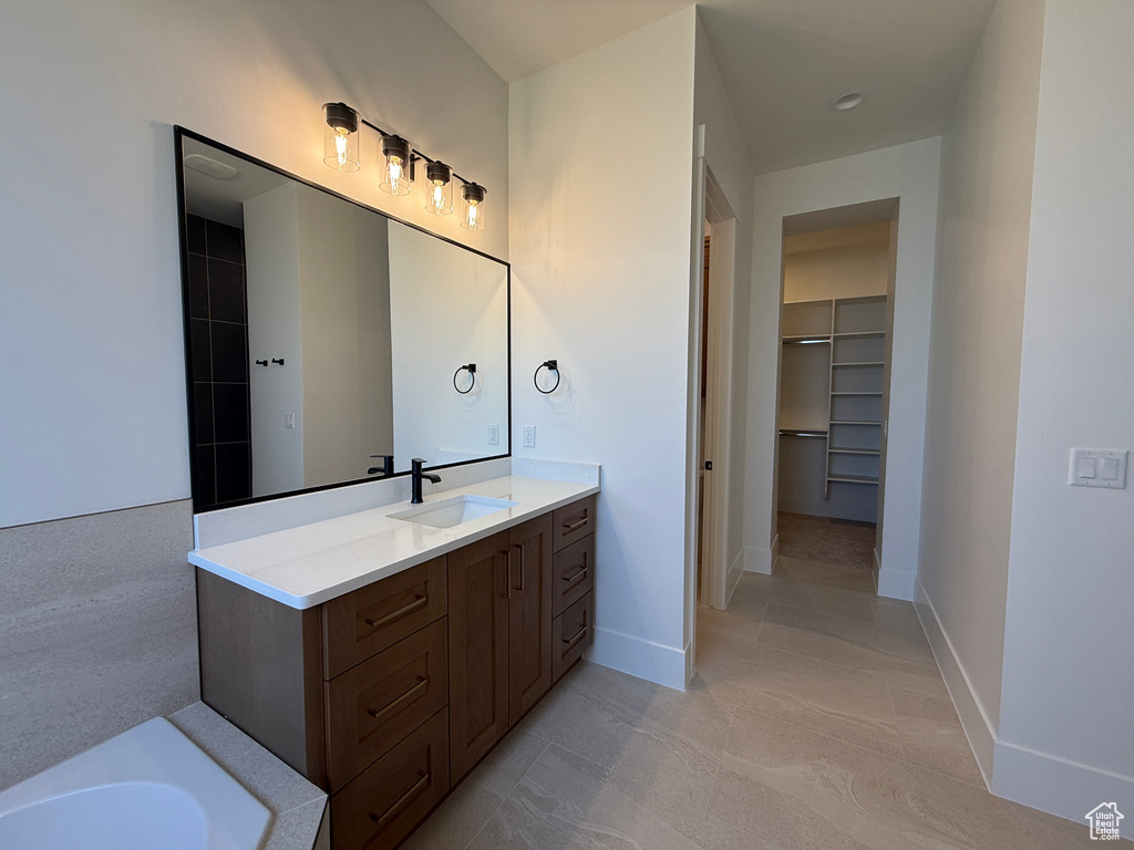 Full bathroom with a spacious closet, vanity, a tub to relax in, baseboards, and tile patterned flooring