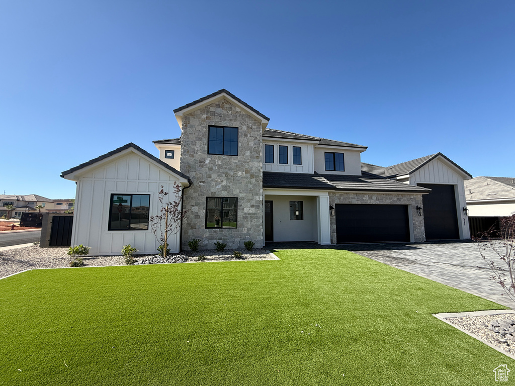 Modern inspired farmhouse with board and batten siding, a front lawn, an attached garage, decorative driveway, and stone siding