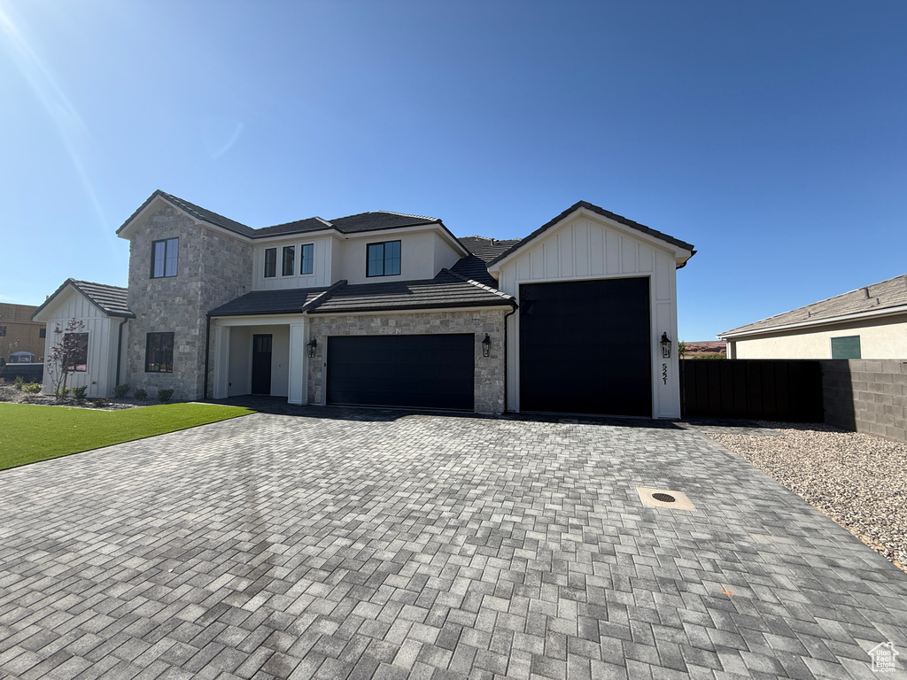 View of front facade with stone siding, fence, decorative driveway, and an attached garage