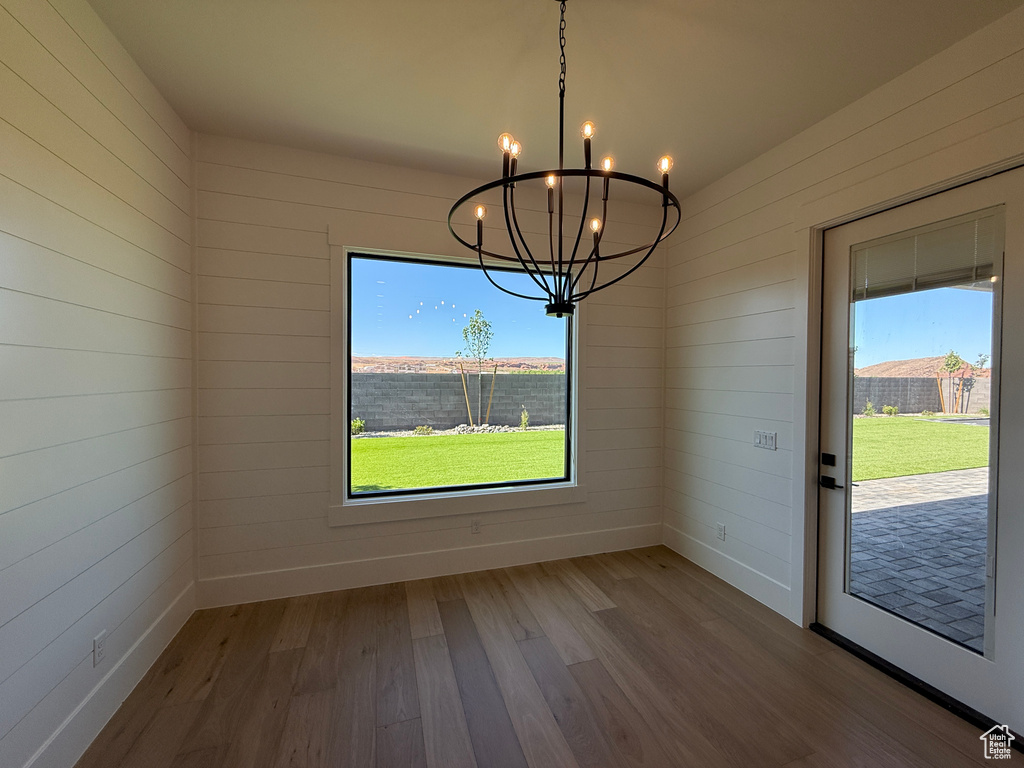 Unfurnished dining area featuring a chandelier, wood finished floors, healthy amount of natural light, baseboards, and wood walls