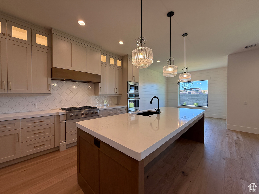 Kitchen with appliances with stainless steel finishes, a sink, light wood-type flooring, decorative backsplash, and recessed lighting