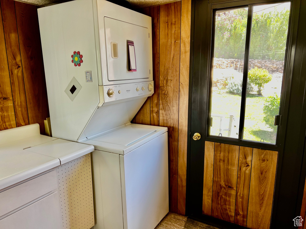 Clothes washing area with stacked washer / dryer, healthy amount of natural light, and wood walls