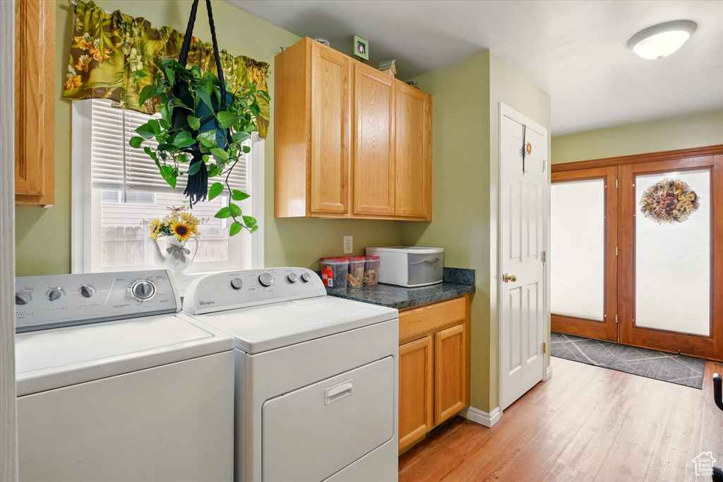 Laundry area with washing machine and dryer, cabinet space, light wood-style floors, and baseboards