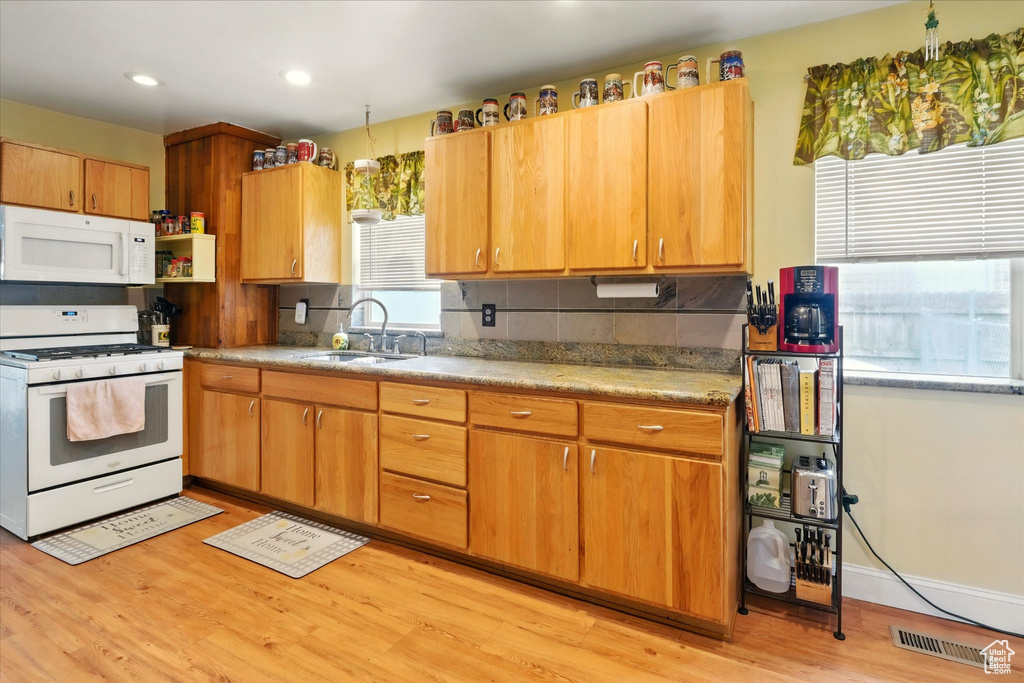 Kitchen with white appliances, a sink, light wood finished floors, backsplash, and recessed lighting