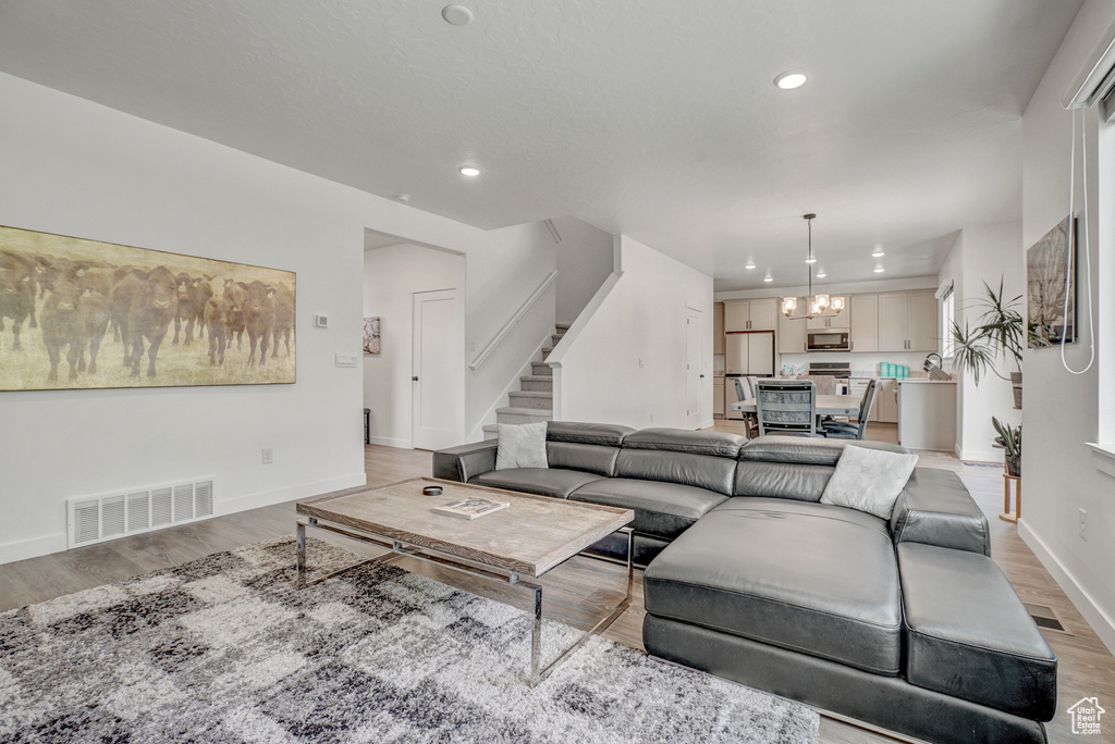 Living area featuring a chandelier, light wood finished floors, stairs, baseboards, and recessed lighting