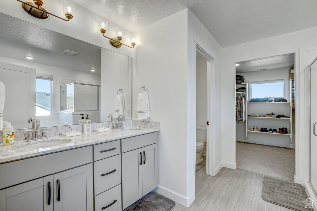Full bathroom featuring toilet, a shower stall, double vanity, baseboards, and a spacious closet