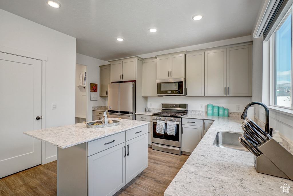 Kitchen featuring appliances with stainless steel finishes, a sink, a center island with sink, wood finished floors, and recessed lighting