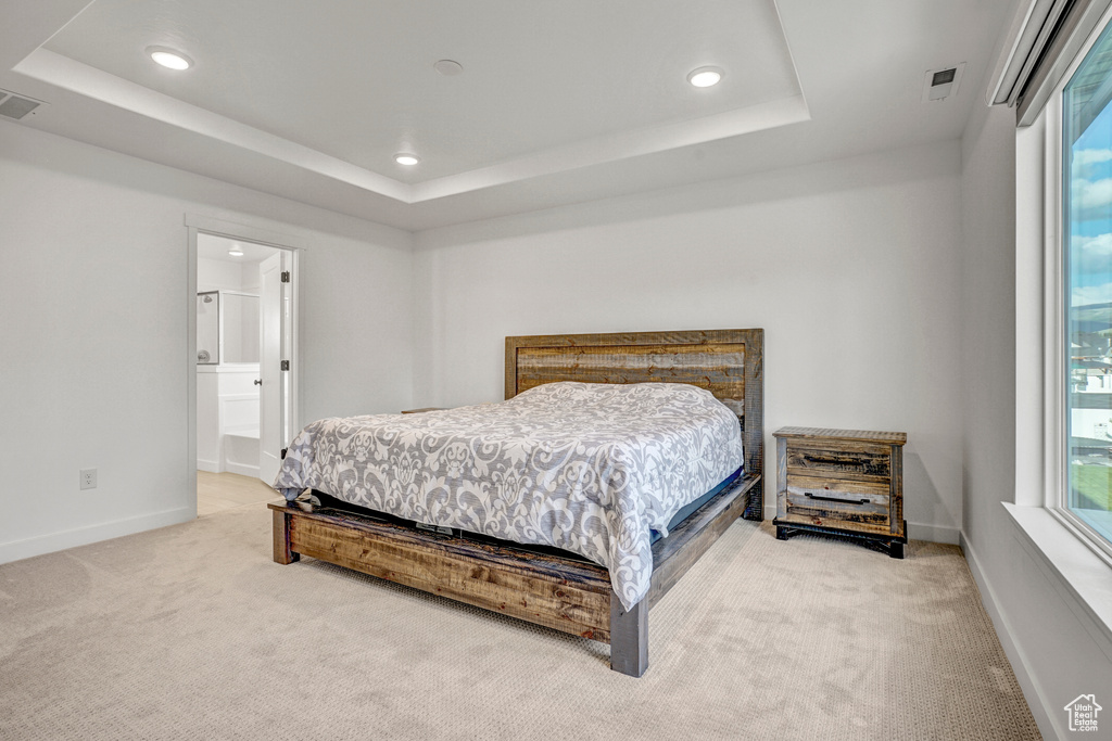 Bedroom with light colored carpet, recessed lighting, a tray ceiling, baseboards, and connected bathroom