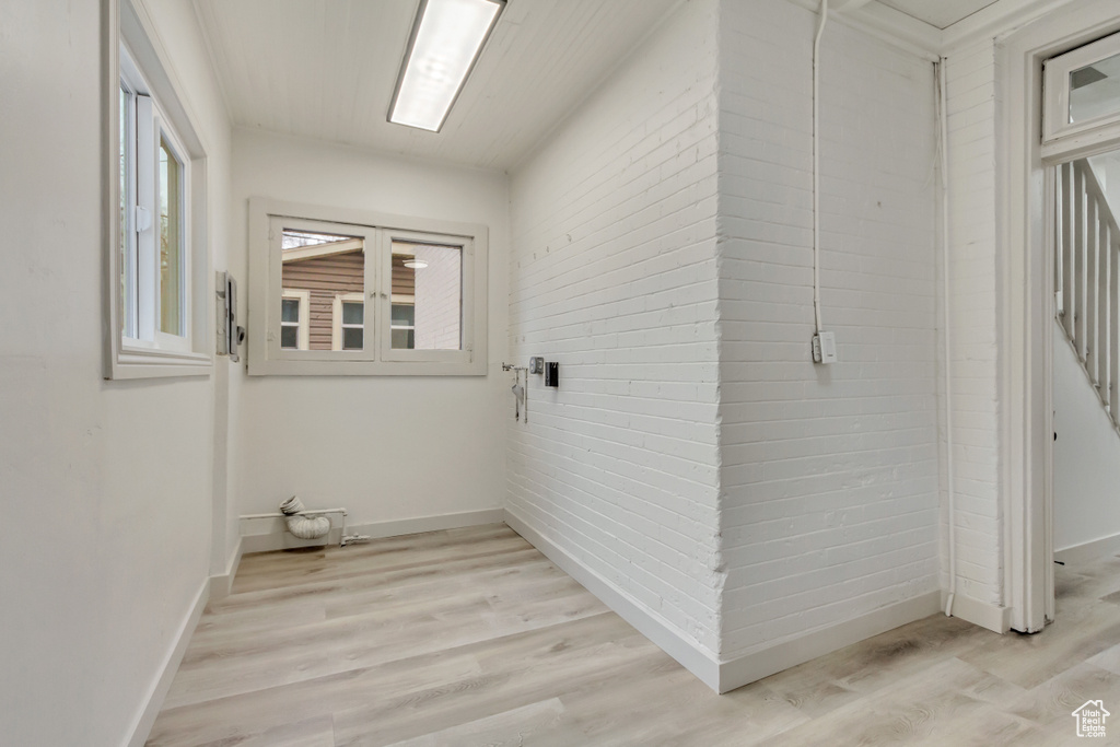 Clothes washing area with light wood-style flooring, baseboards, and brick wall