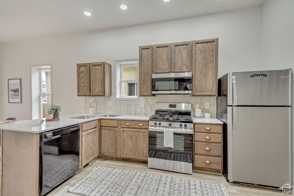 Kitchen with appliances with stainless steel finishes, a sink, backsplash, light wood-style flooring, and light countertops