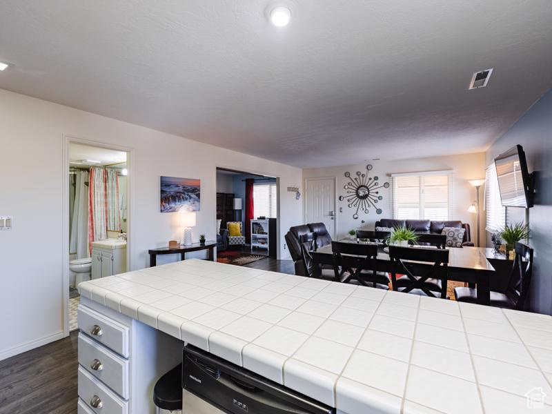 Kitchen featuring open floor plan, dishwasher, tile counters, dark wood-style flooring, and baseboards