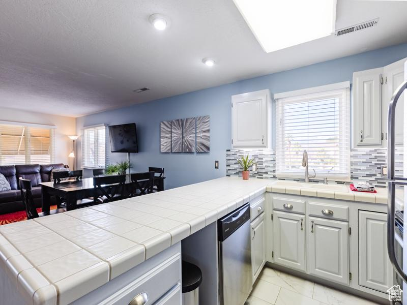 Kitchen featuring dishwasher, open floor plan, a sink, a peninsula, and tasteful backsplash