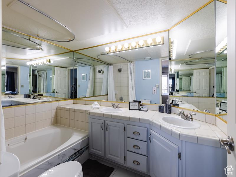 Bathroom with a shower with curtain, a bath, double vanity, and a textured ceiling