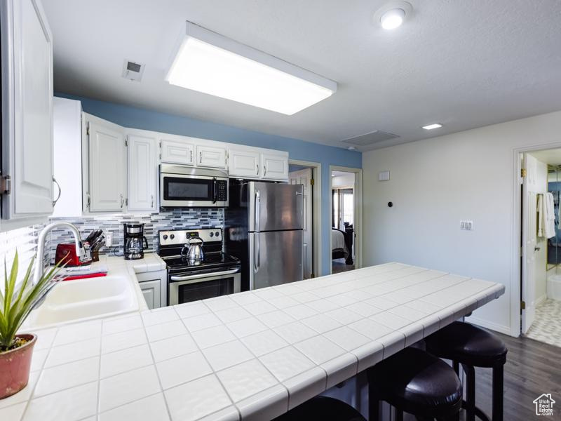 Kitchen with appliances with stainless steel finishes, a sink, backsplash, a peninsula, and tile counters