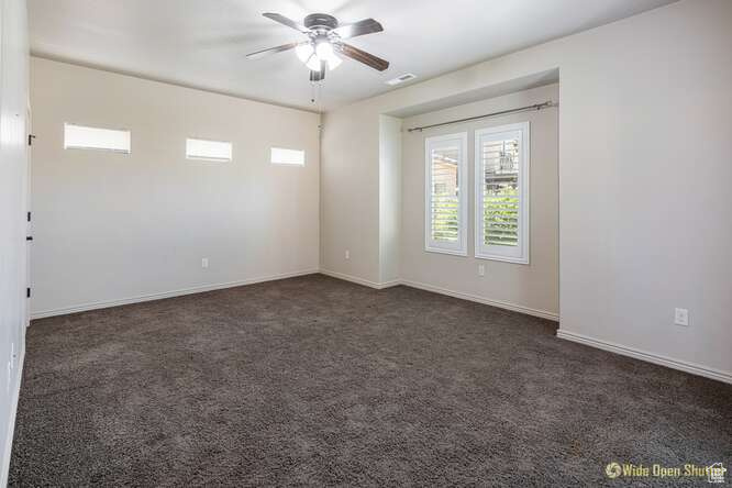 Unfurnished room with a ceiling fan, dark colored carpet, and baseboards