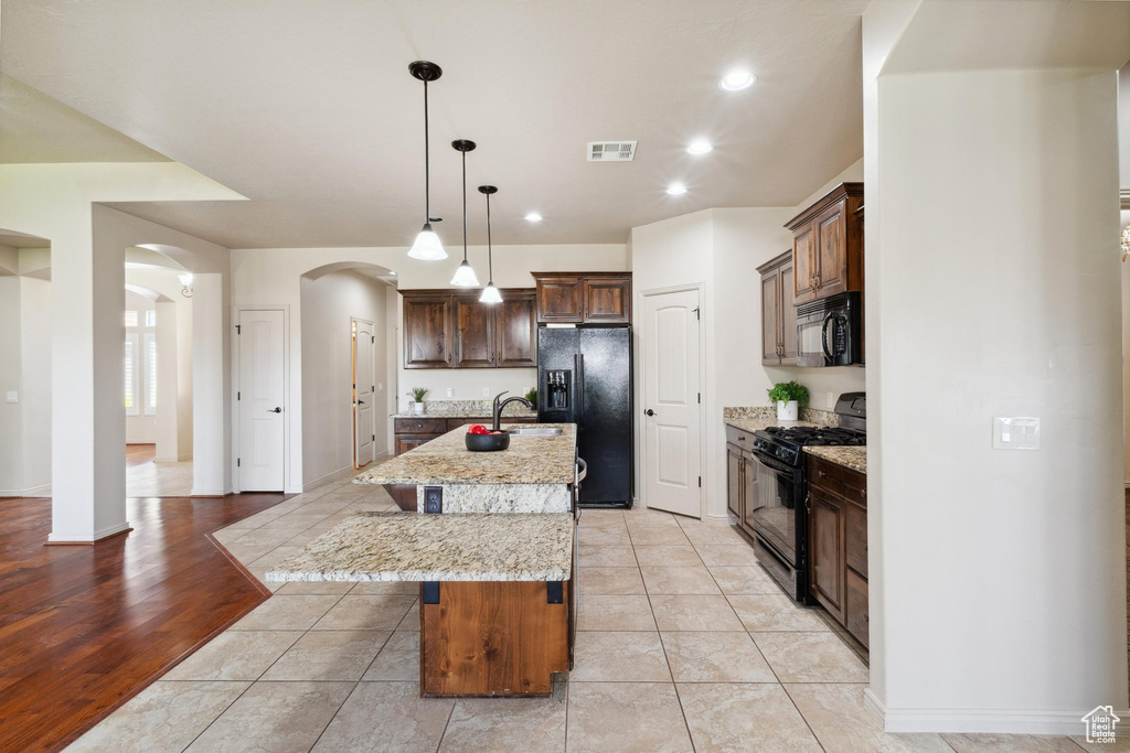 Kitchen featuring black appliances, arched walkways, a breakfast bar area, a sink, and an island with sink