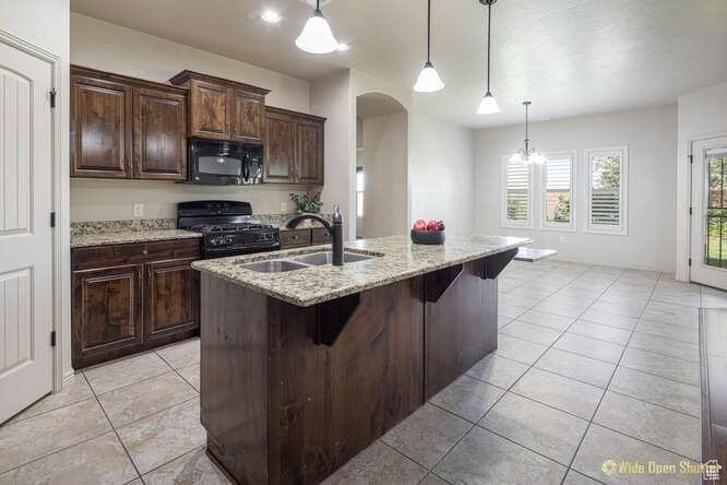 Kitchen featuring black appliances, a sink, arched walkways, light tile patterned floors, and a breakfast bar