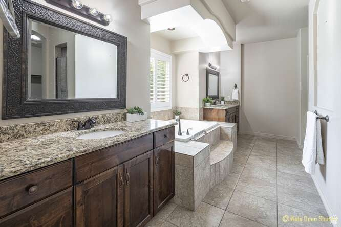 Full bath with two vanities, a bath, and baseboards