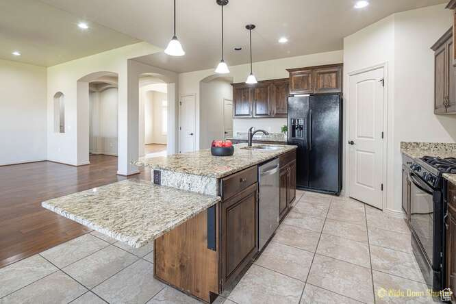 Kitchen with black appliances, arched walkways, a sink, an island with sink, and recessed lighting