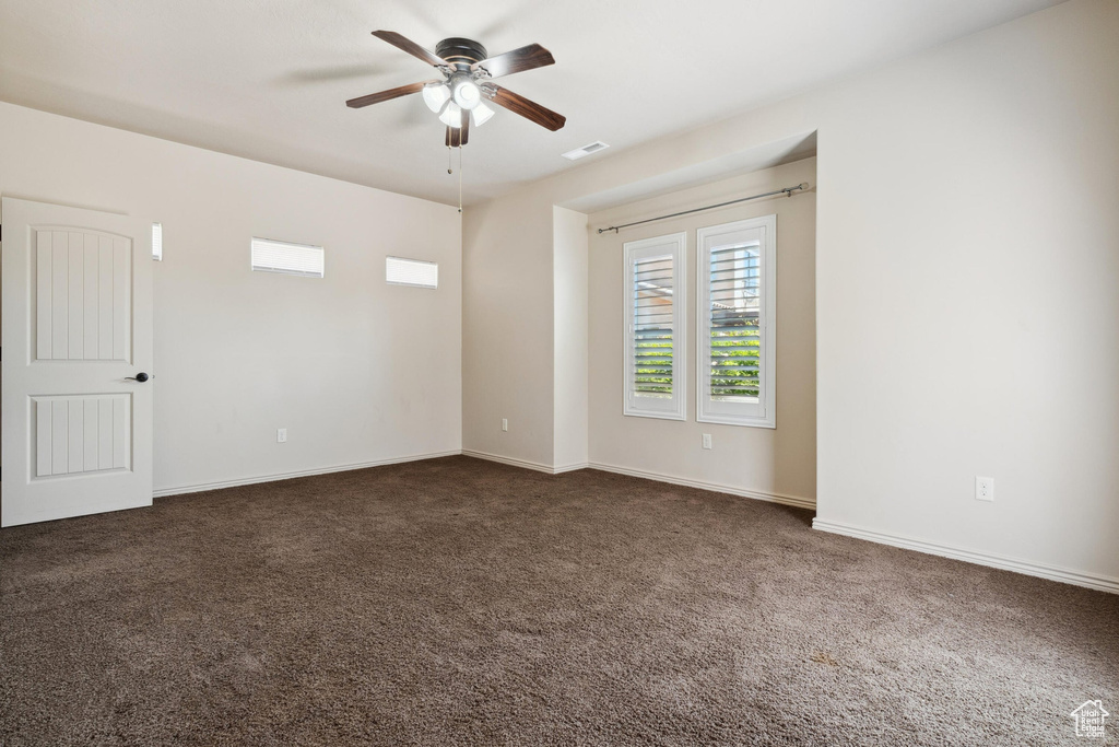 Spare room with ceiling fan, dark carpet, and baseboards