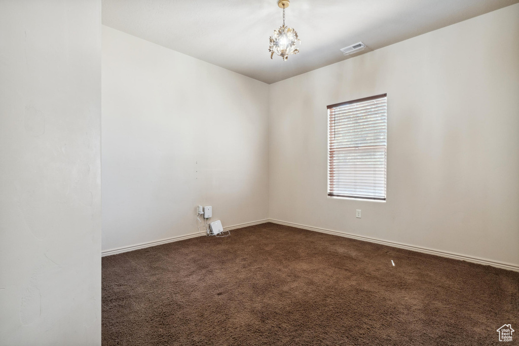 Unfurnished room featuring dark colored carpet, a chandelier, and baseboards