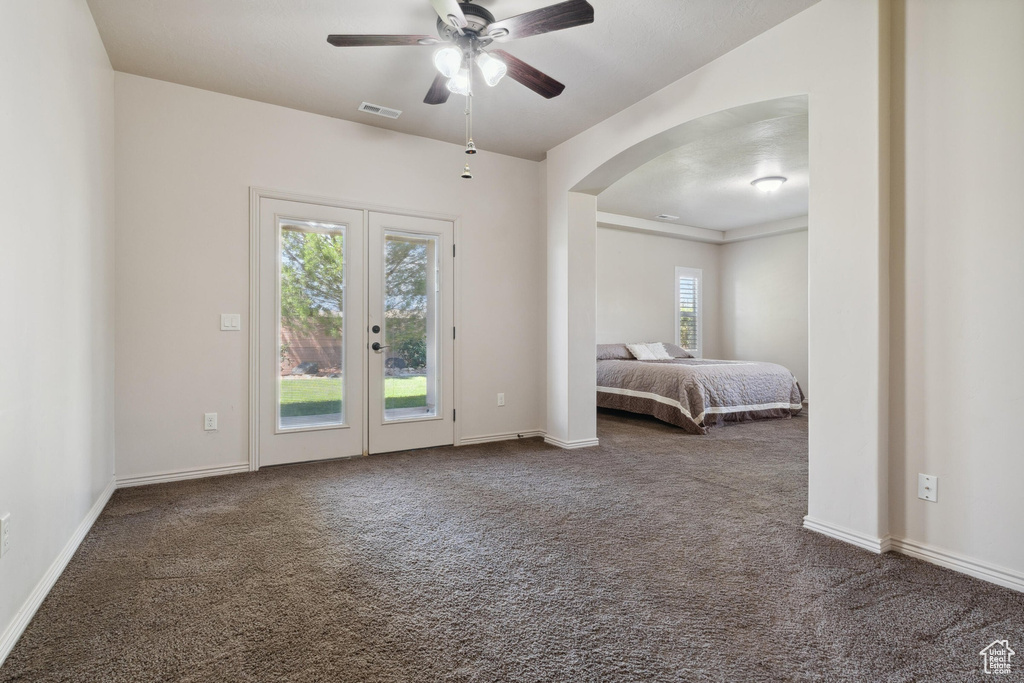 Bedroom featuring access to exterior, dark carpet, french doors, arched walkways, and a ceiling fan