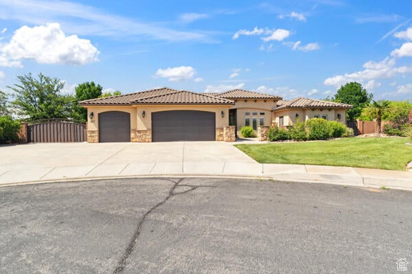 Mediterranean / spanish-style home with stucco siding, stone siding, a garage, driveway, and a tile roof