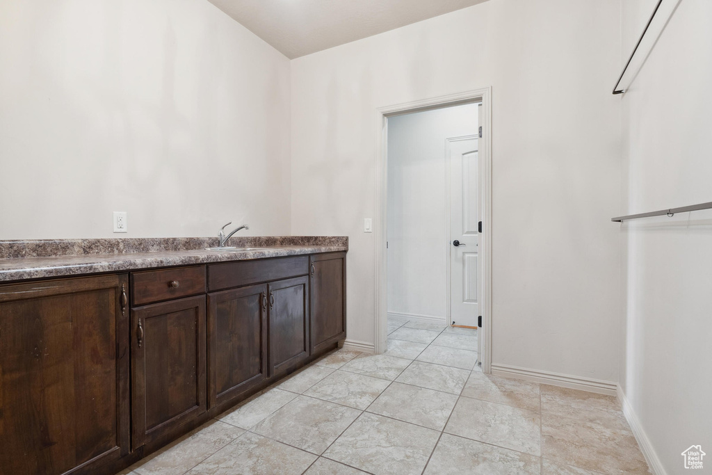 Kitchen featuring dark brown cabinetry, a sink, baseboards, and light tile patterned flooring