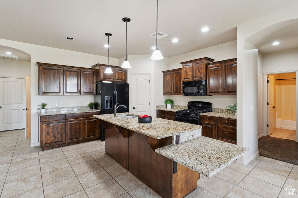 Kitchen featuring black appliances, arched walkways, a kitchen island with sink, a kitchen breakfast bar, and dark brown cabinets