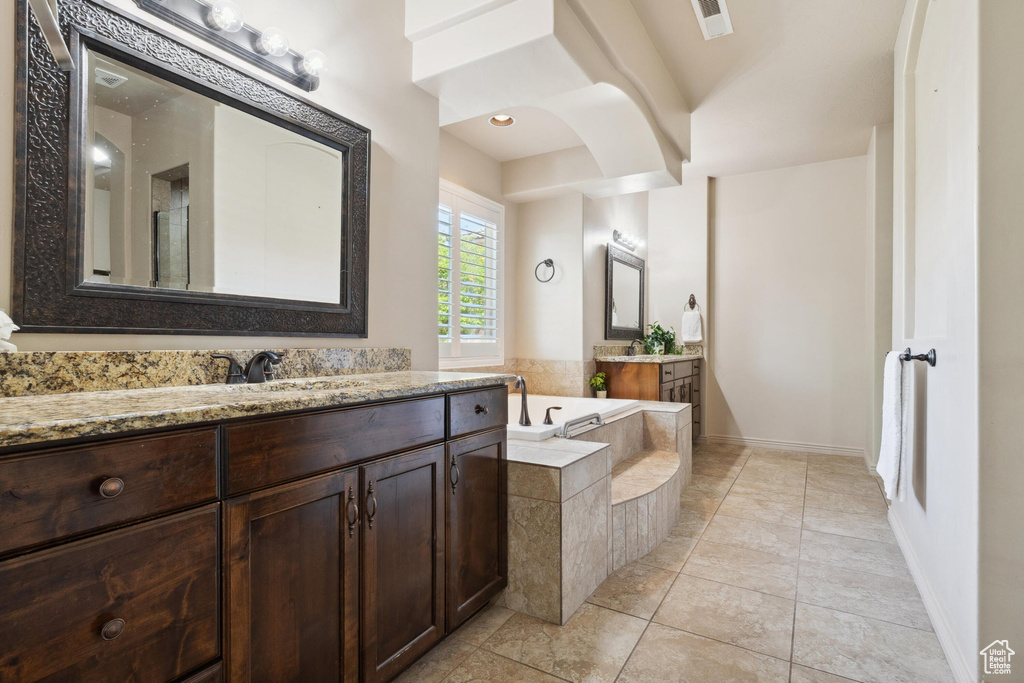 Full bathroom featuring two vanities, a garden tub, baseboards, and tile patterned flooring