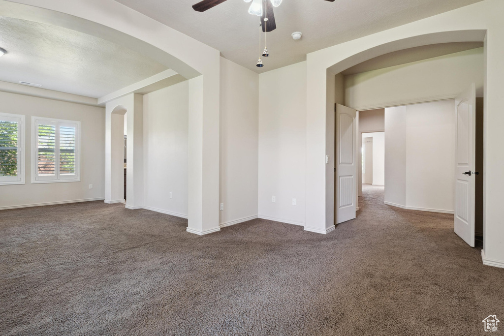 Empty room with dark carpet, a ceiling fan, arched walkways, and baseboards