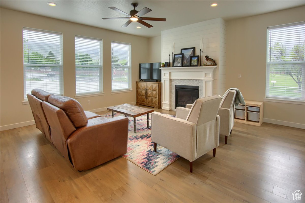 Living room featuring baseboards, light wood-style flooring, ceiling fan, a glass covered fireplace, and recessed lighting