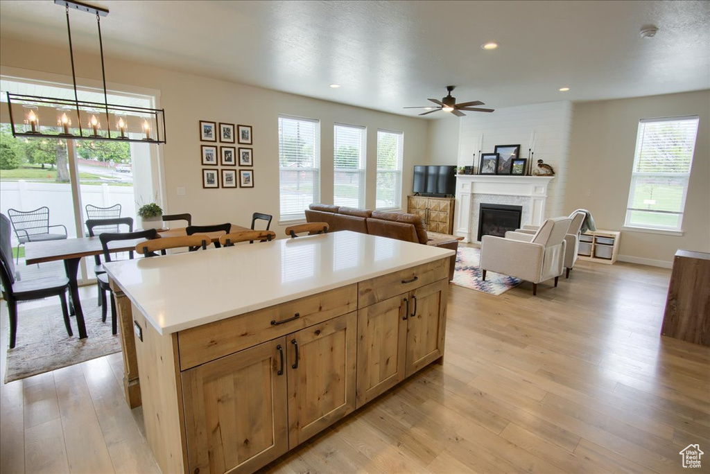 Kitchen featuring light wood finished floors, a chandelier, a glass covered fireplace, a ceiling fan, and hanging light fixtures
