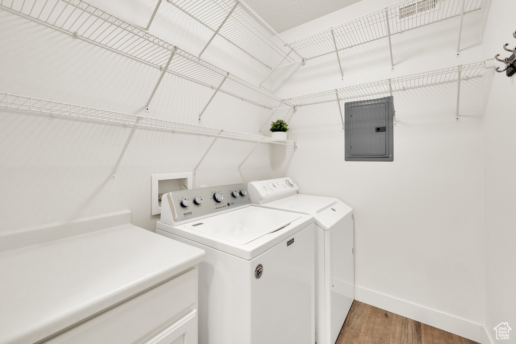 Laundry room featuring electric panel, washer and dryer, baseboards, and wood finished floors