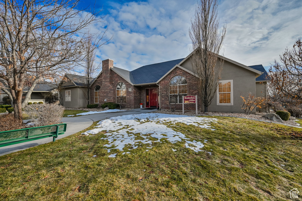 View of front of house with brick siding, a chimney, a front yard, and stucco siding