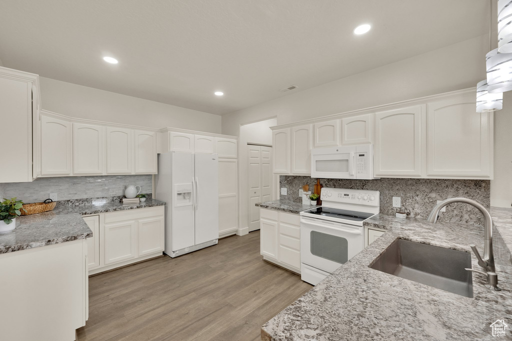 Kitchen with white appliances, a sink, tasteful backsplash, light stone counters, and white cabinets