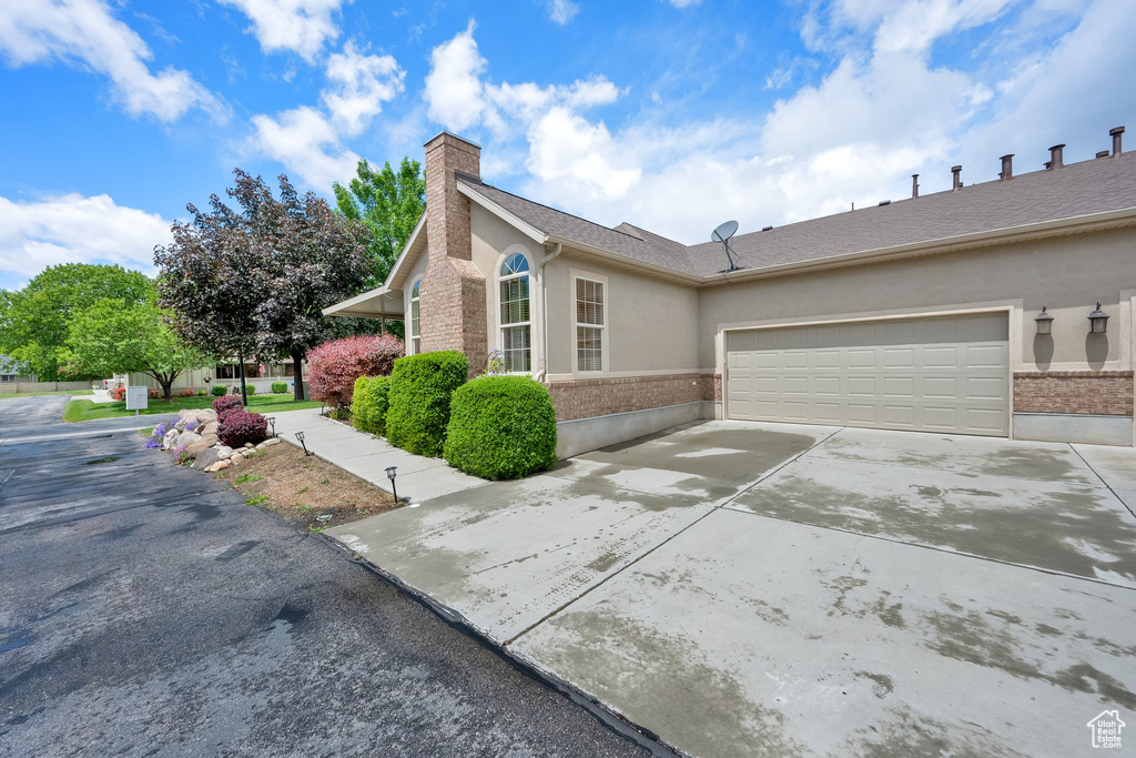 View of side of property featuring stucco siding, a chimney, concrete driveway, brick siding, and a garage