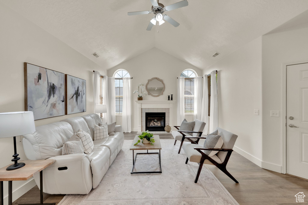 Living room featuring a ceiling fan, a tiled fireplace, light wood-style floors, lofted ceiling, and baseboards