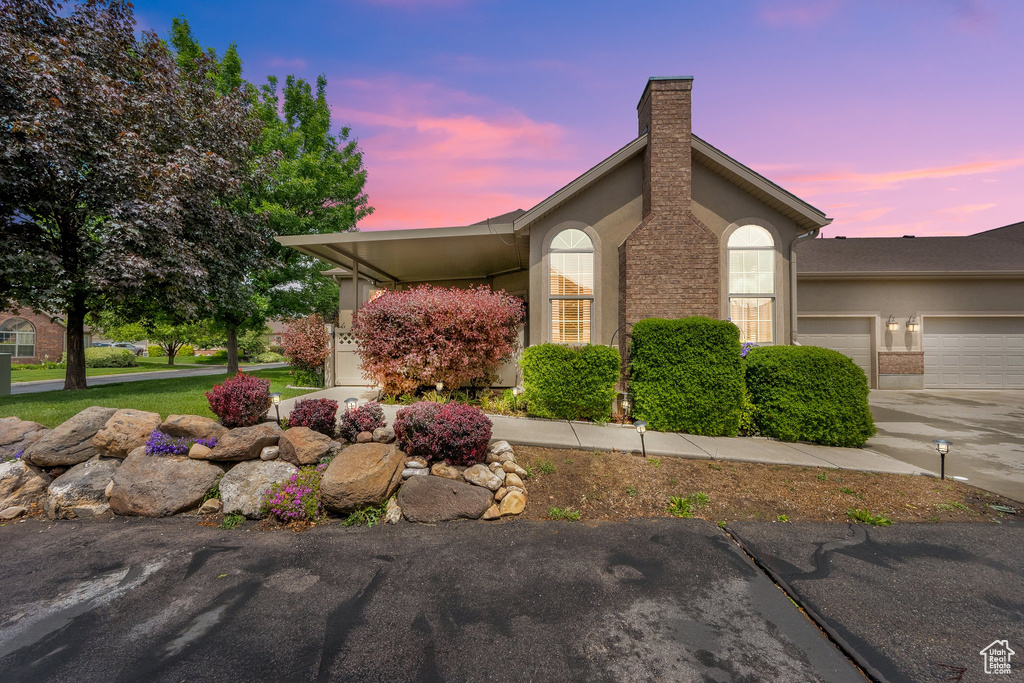 Property exterior at dusk featuring a chimney, concrete driveway, a garage, and stucco siding