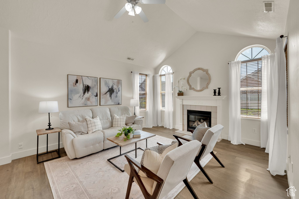 Living area featuring plenty of natural light, vaulted ceiling, a fireplace, wood finished floors, and ceiling fan