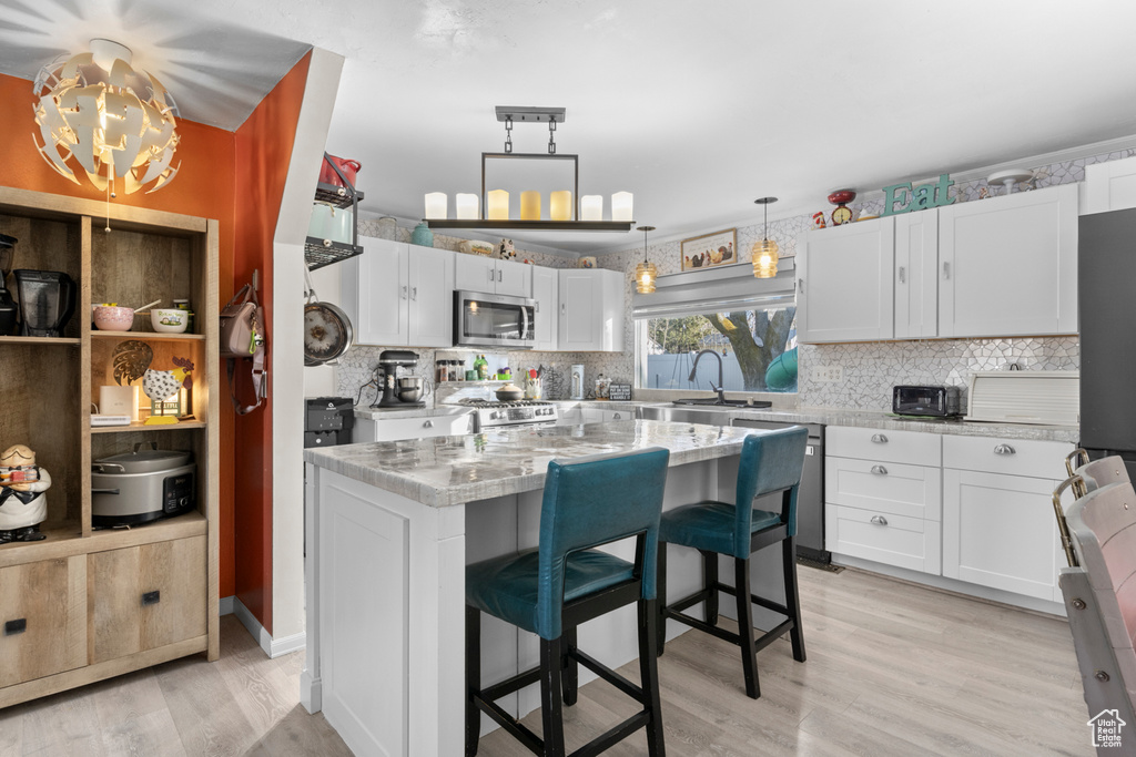 Kitchen featuring appliances with stainless steel finishes, light wood-type flooring, decorative backsplash, and white cabinetry
