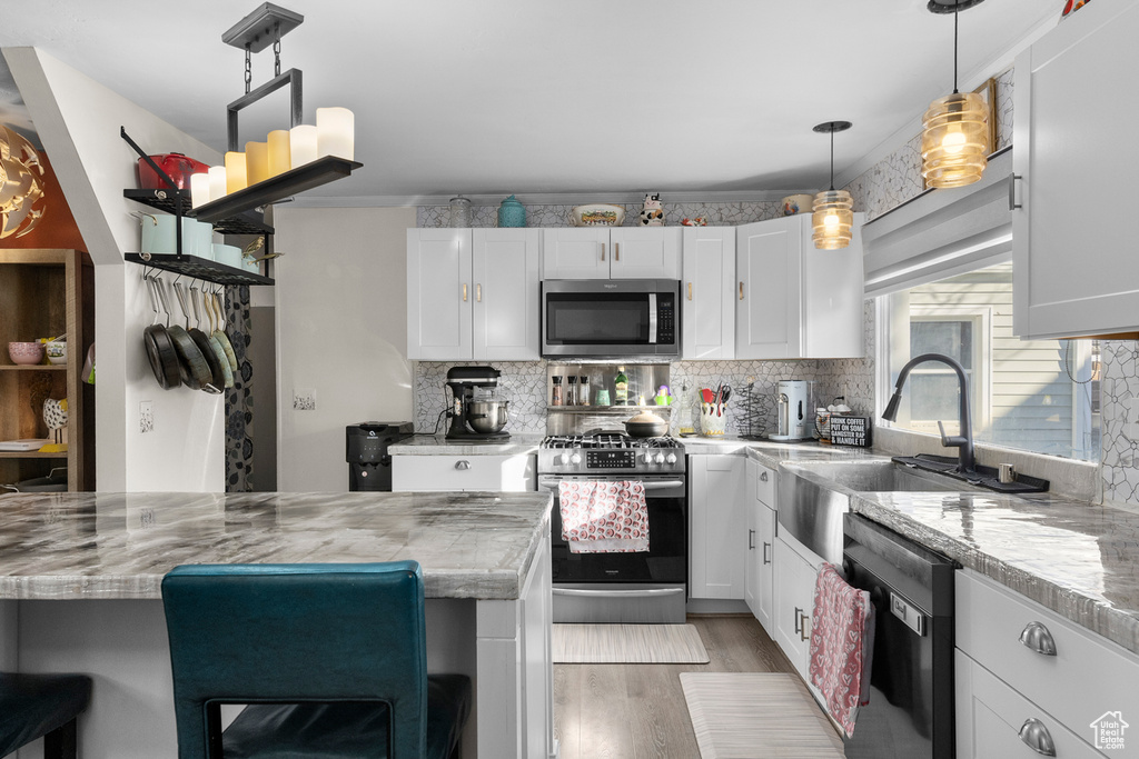Kitchen featuring appliances with stainless steel finishes, light wood finished floors, white cabinets, tasteful backsplash, and a kitchen breakfast bar