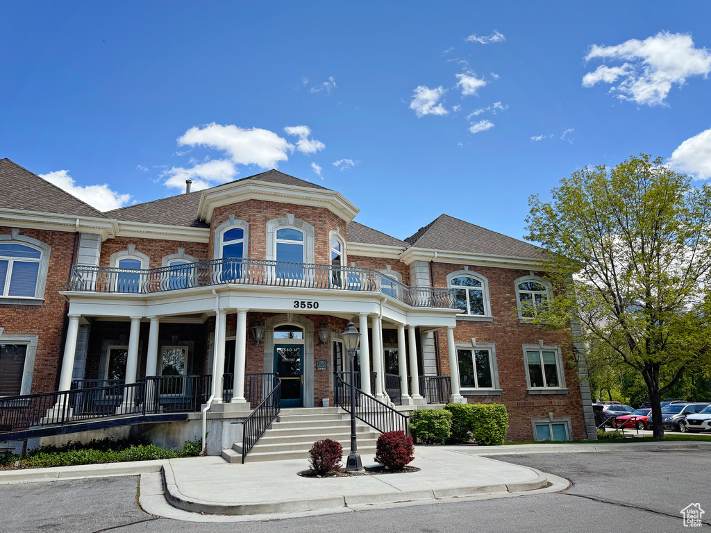 View of front of house featuring brick siding, a balcony, covered porch, and a shingled roof