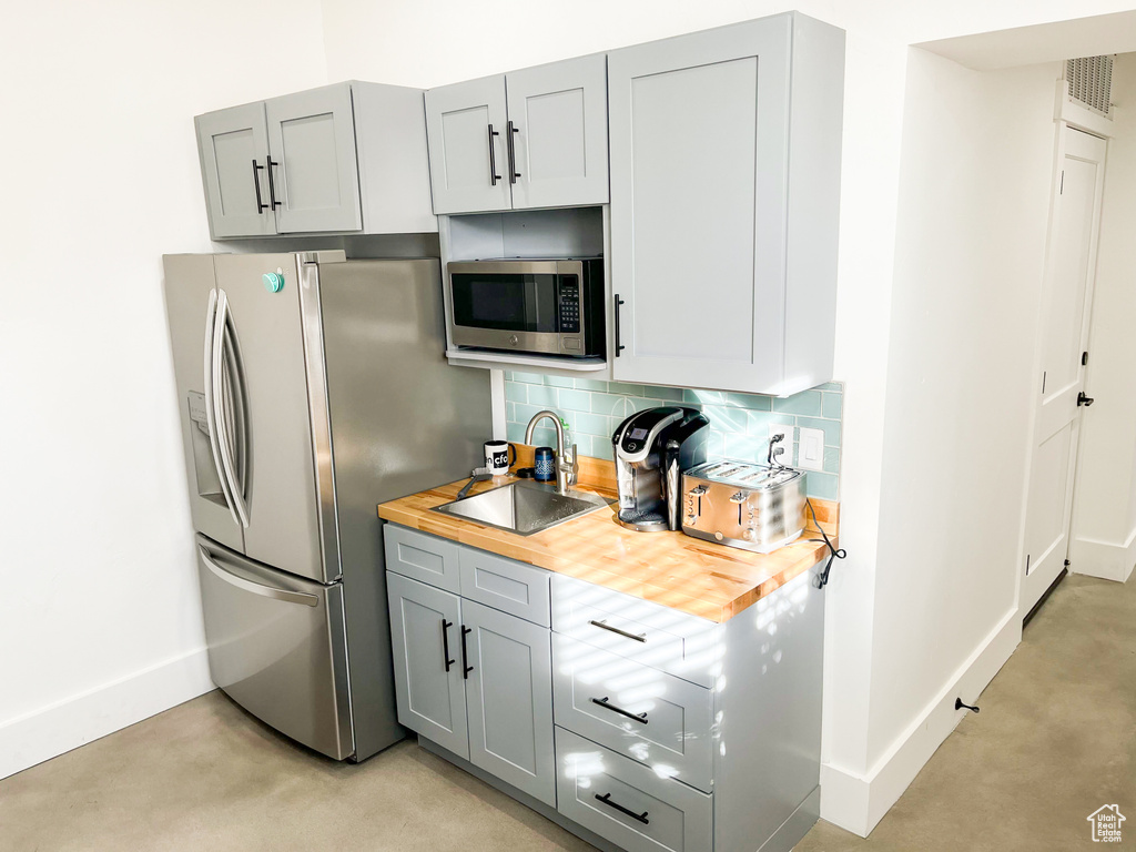 Kitchen with appliances with stainless steel finishes, a sink, butcher block countertops, baseboards, and finished concrete flooring