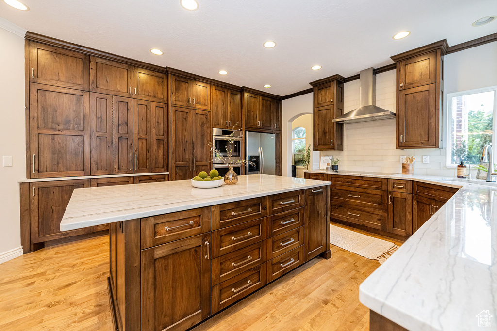 Kitchen featuring wall chimney range hood, appliances with stainless steel finishes, a sink, arched walkways, and ornamental molding