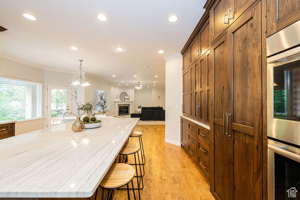 Kitchen with crown molding, recessed lighting, light wood-type flooring, a kitchen breakfast bar, and light stone counters